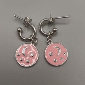 Aros de plata de ley con estrellas y luna en relieve sobre fondo en color rosa,