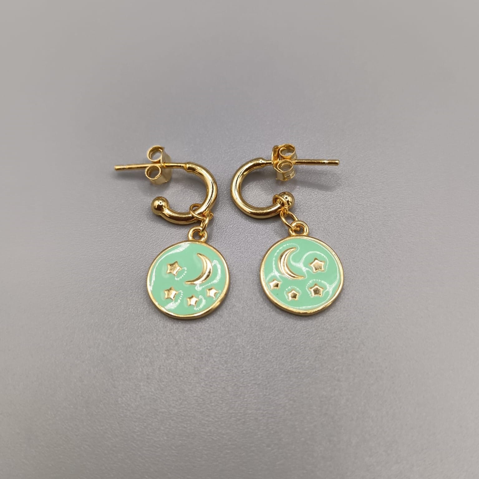 Pendientes en plata de ley, aros montados con palillo y cierre presion cuelga de ellos un colgante con estrella y luna en relieve sobre esmaltado en color verde agua