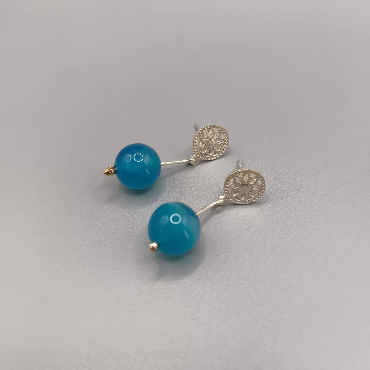 Pendientes en plata de ley montados con un roseton calado, palillo articulado y agata natural color azul